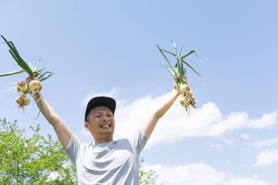 A young man holding up freshly harvested onions against a blue sky